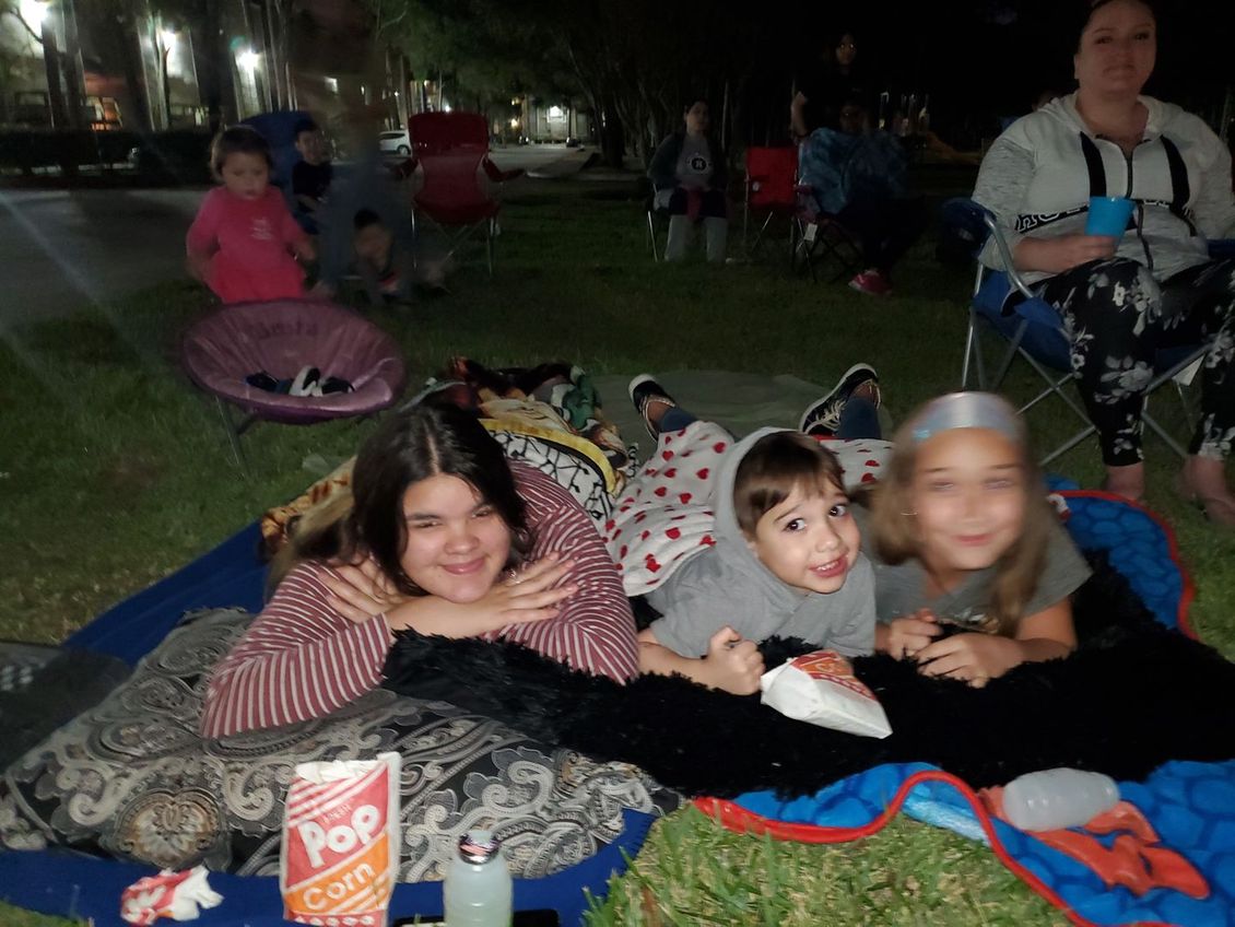 A group of children are laying on a blanket in the grass with a box of pop corn in the foreground.