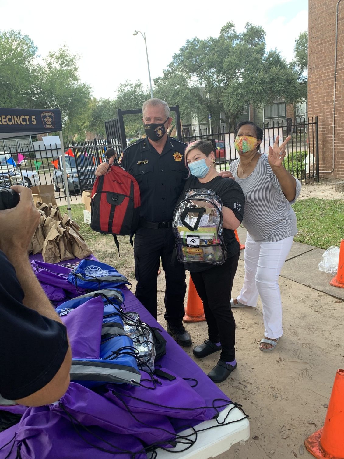 A group of people wearing face masks are standing in front of a table full of backpacks.