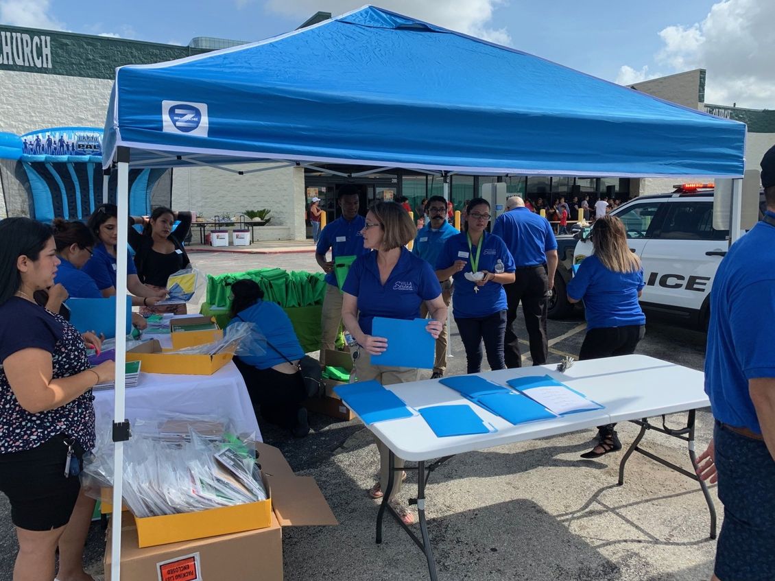 A group of people standing around a table under a blue tent.