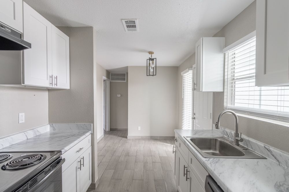 a kitchen with white cabinets , a stove , a sink , and a window .