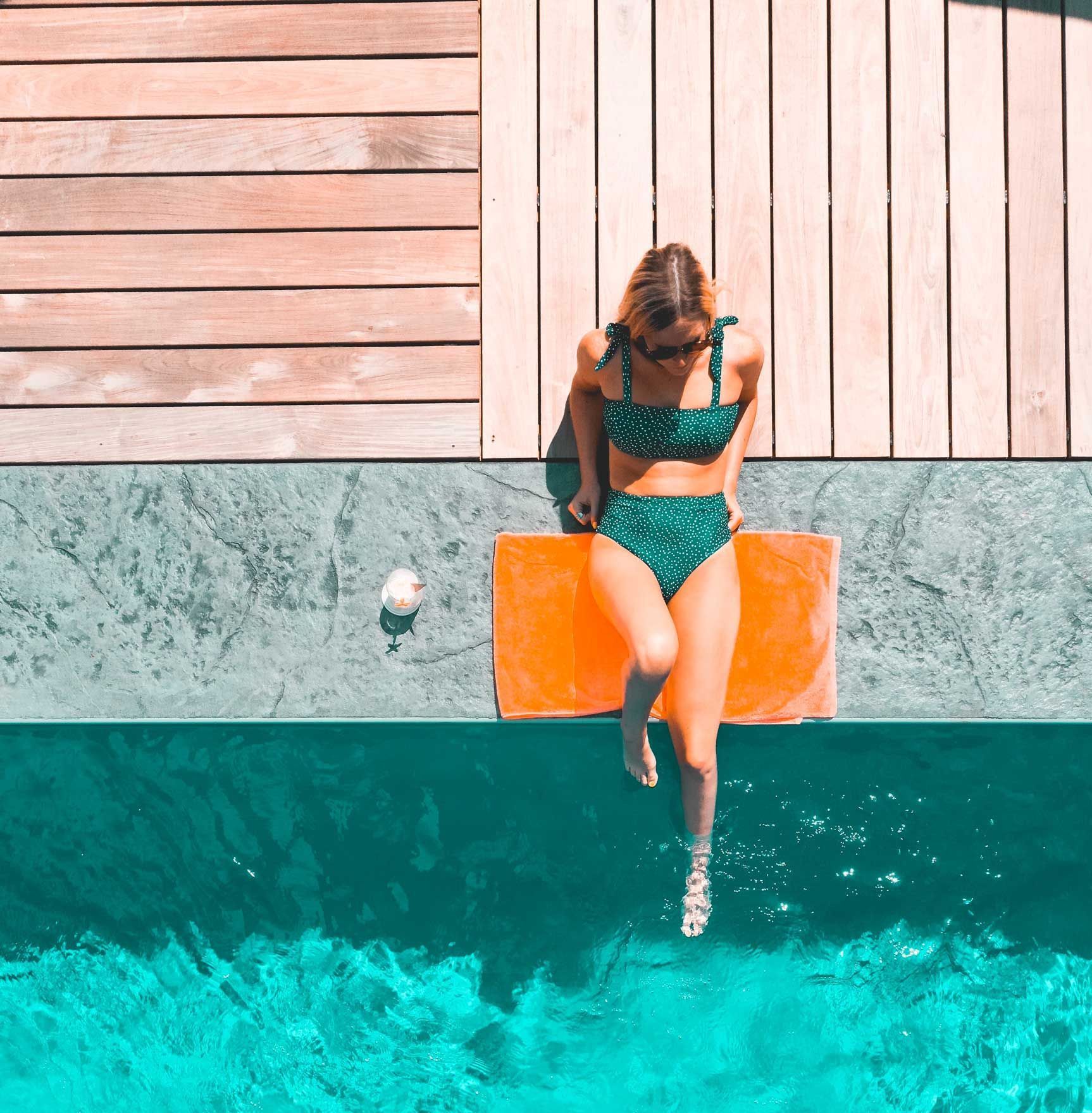 a woman in a bikini is sitting on the edge of a swimming pool .
