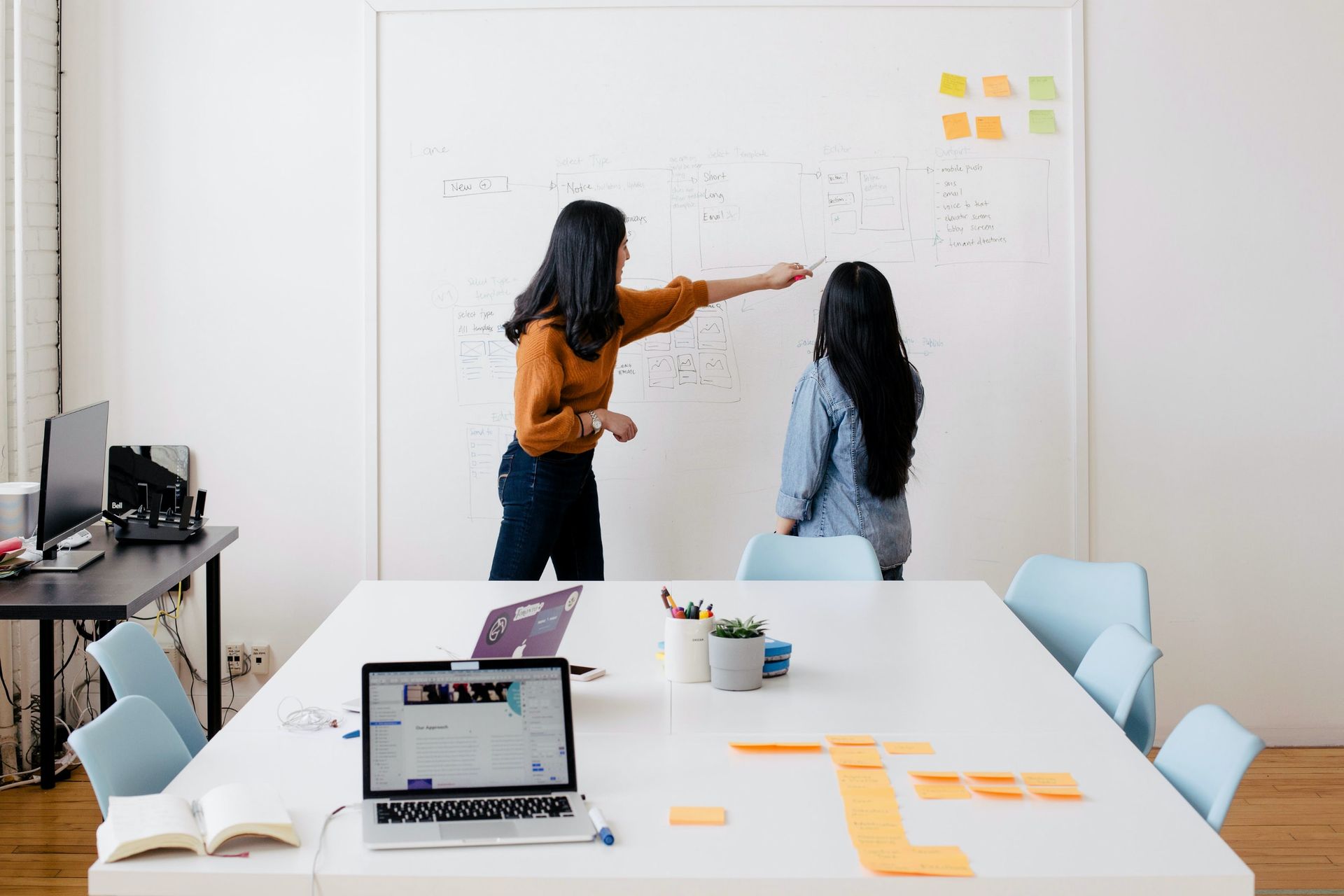 two women are standing in front of a whiteboard in a conference room .