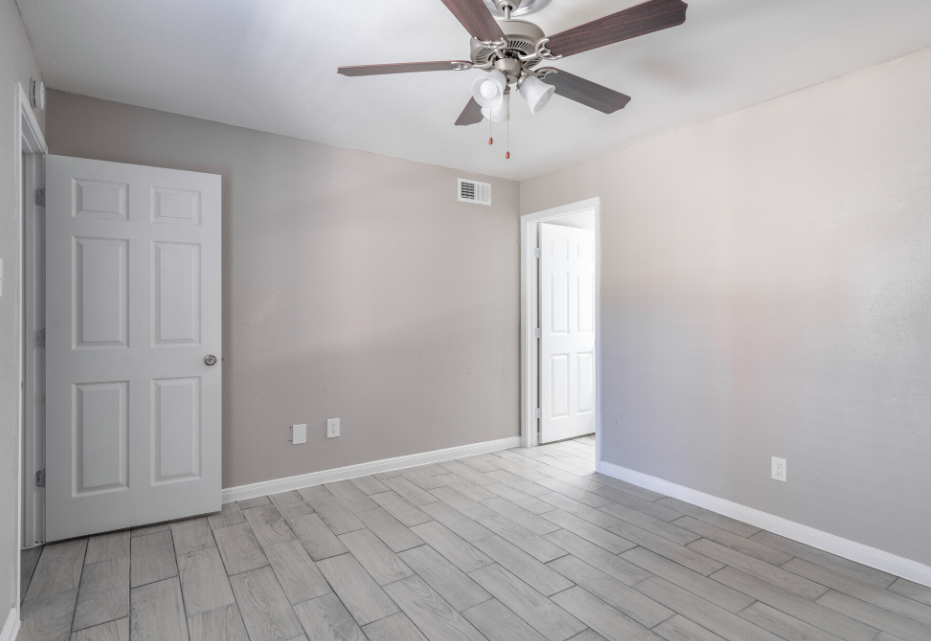 An empty bedroom with a ceiling fan and a door.