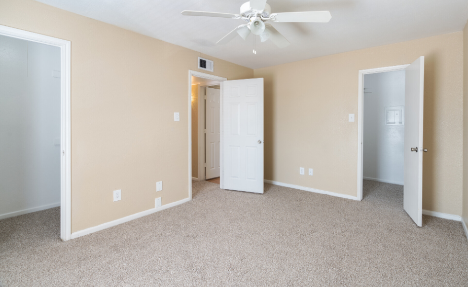 An empty bedroom with a ceiling fan and two doors.
