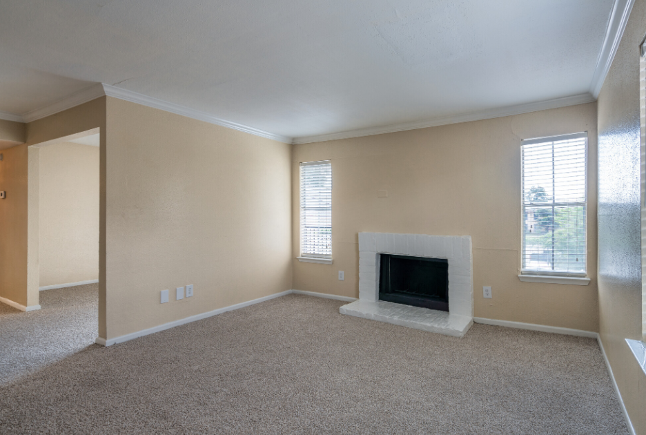 An empty living room with a fireplace and two windows.