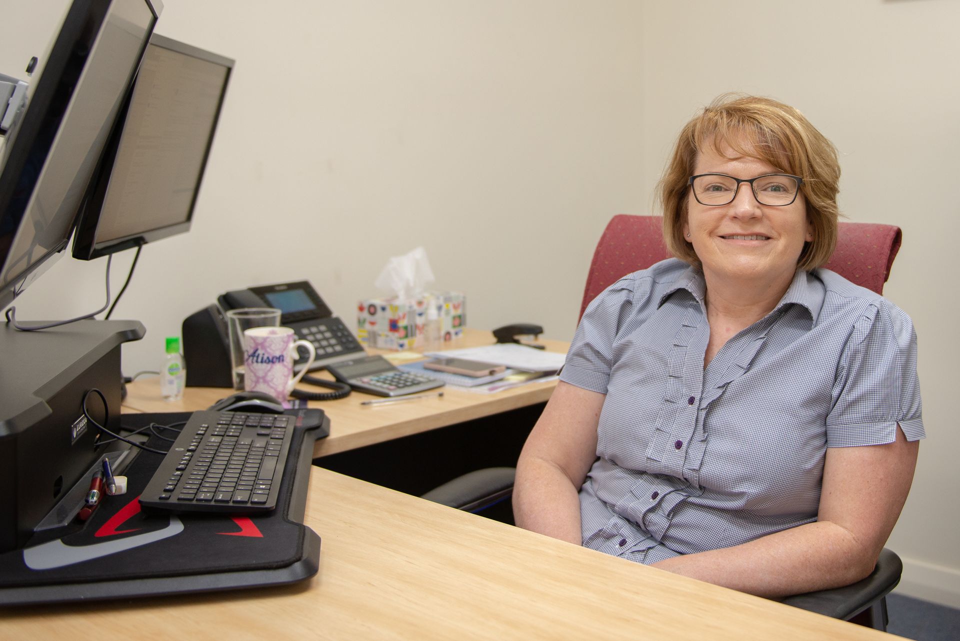 Woman in office, sitting at desk, smiling. Computers and phone visible — Wright Partners in Dubbo, NSW