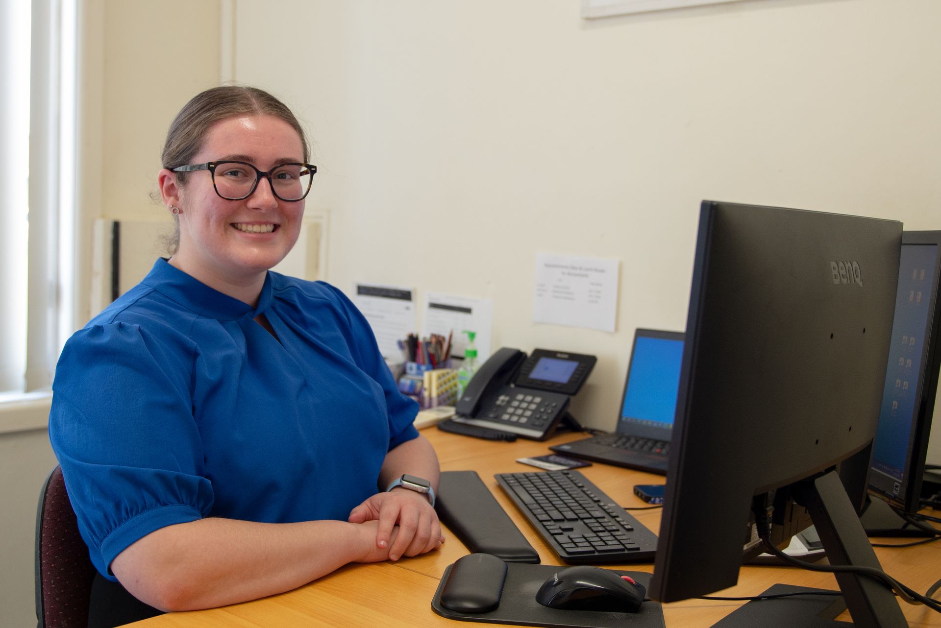 Woman in blue shirt smiles at desk with computer and phone — Wright Partners in Dubbo, NSW