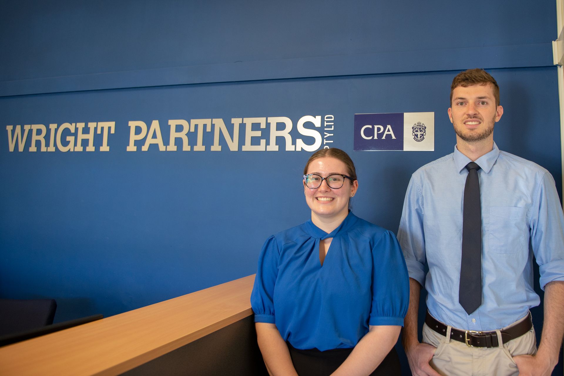 Woman in A Blue Shirt Sits at A Desk with A Computer, Smiling at The Camera — Wright Partners in Dubbo, NSW
