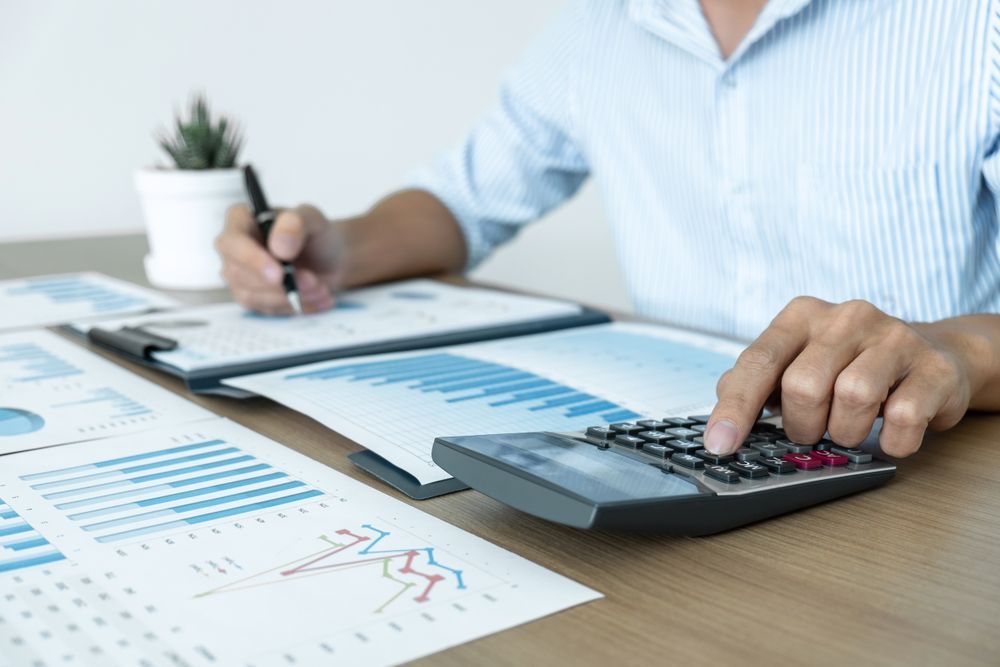 Person Using a Calculator, Writing on A Clipboard, and Reviewing Financial Graphs on A Desk — Wright Partners in Bourke, NSW
