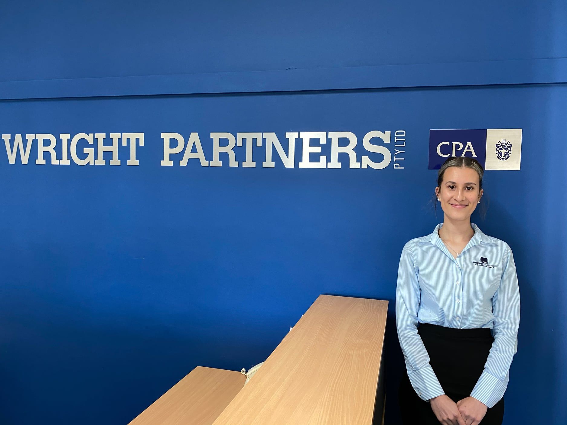 Woman Standing in Front of A Blue Wall with Wright Partners Sign and CPA Logo — Wright Partners in Dubbo, NSW