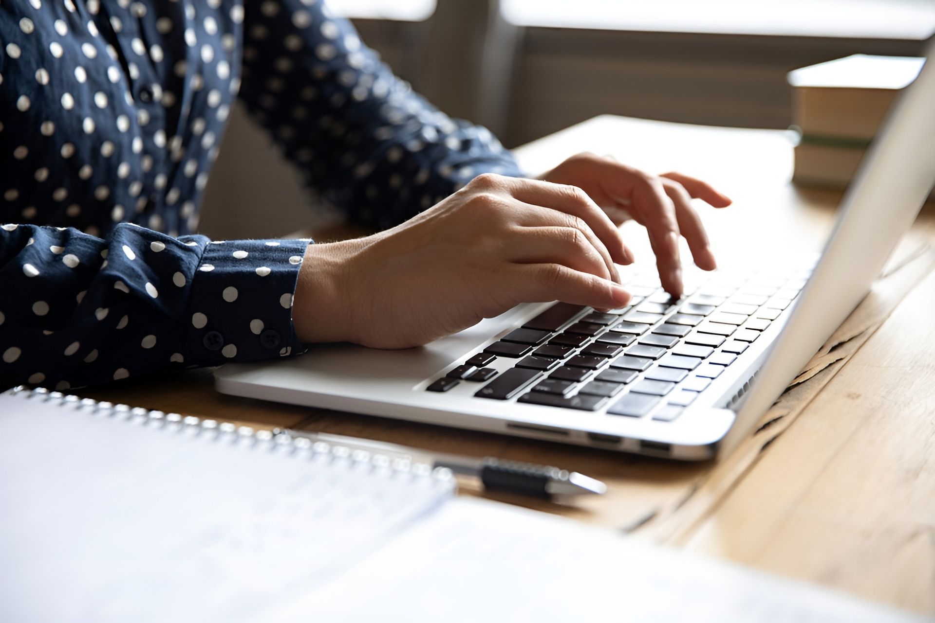 Person Typing on A Laptop at A Desk; Hands on The Keyboard, Notebook and Pen Visible — Wright Partners in Bourke, NSW
