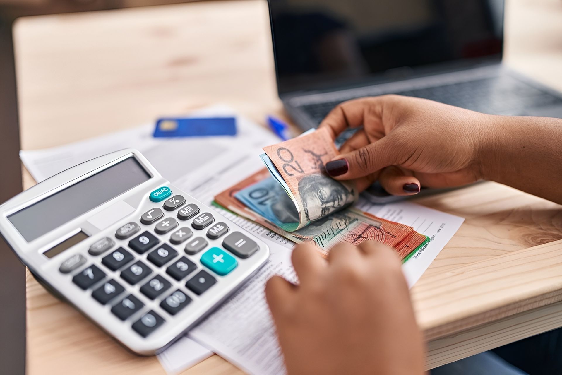 Hands Counting Australian Banknotes Next to A Calculator, Bills, And A Laptop — Wright Partners in Cobar, NSW
