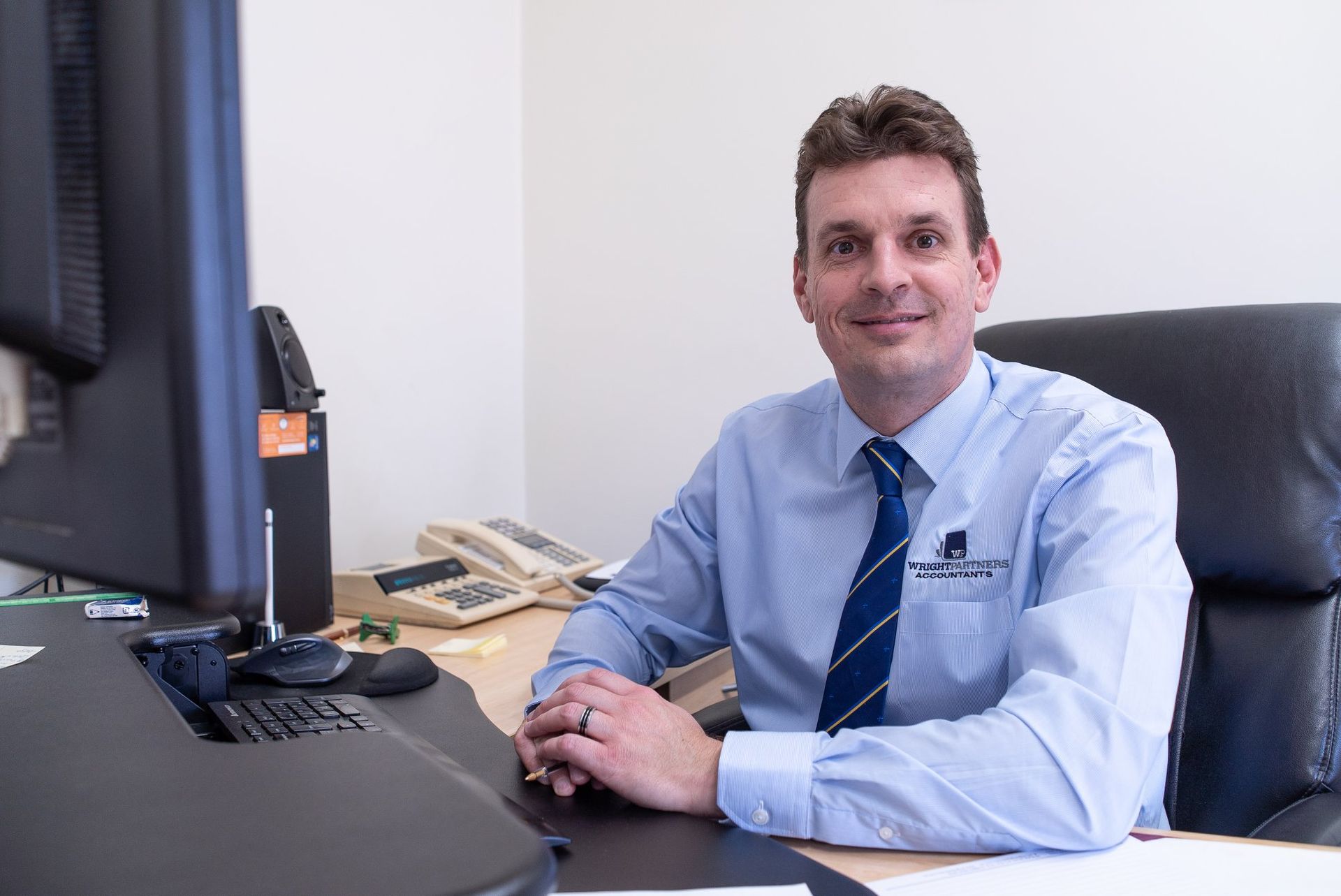 Man in Blue Shirt and Tie Sits at Desk in Office, Smiling at The Camera — Wright Partners in Dubbo, NSW