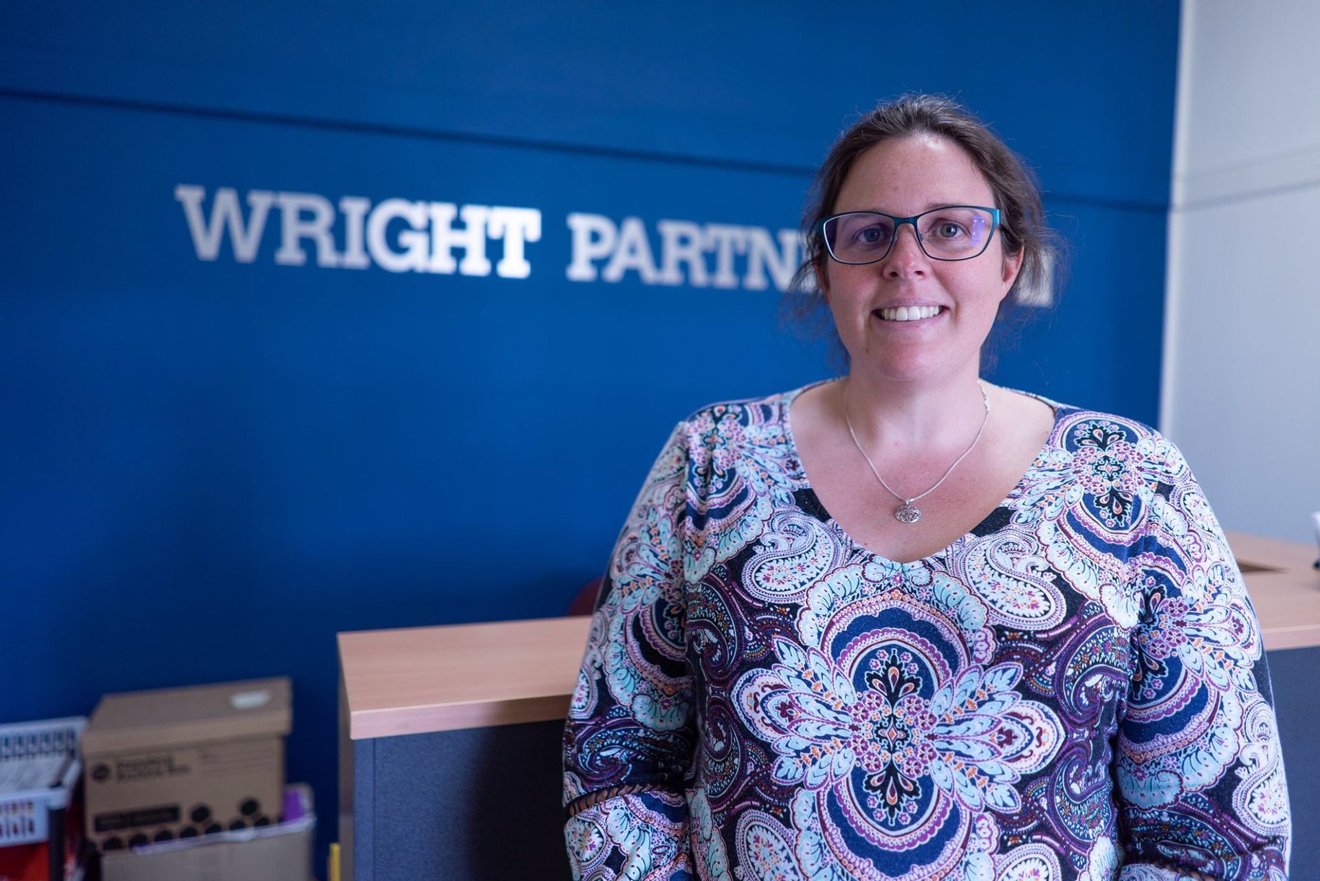 Woman with Glasses Smiles in Front of A Blue Wall with Wright Partners — Wright Partners in Dubbo, NSW