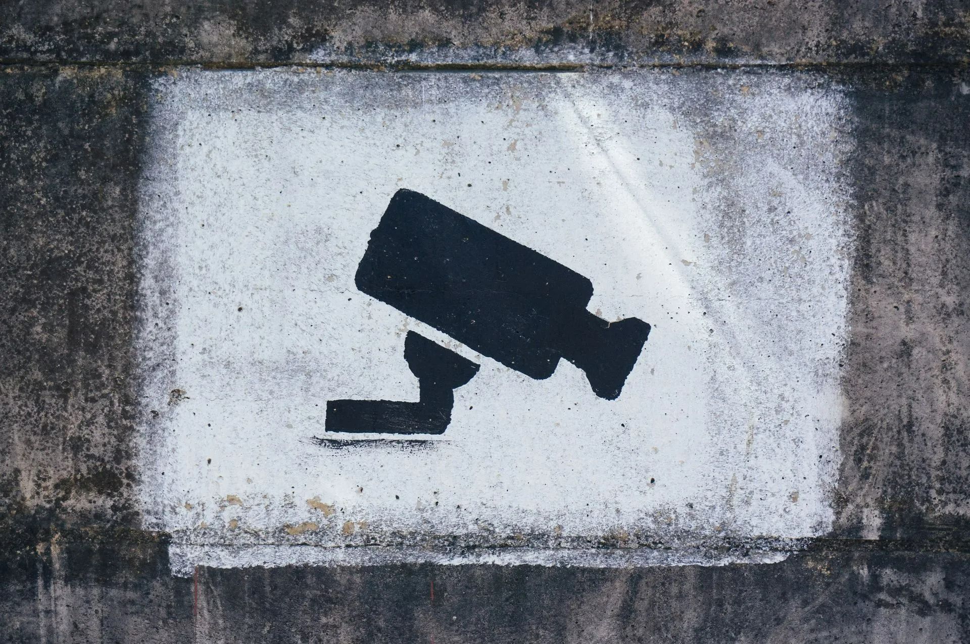Black Security Camera Symbol Stencilled on White Rectangle, Set Against a Dark Wall — Wright Partners in Dubbo, NSW
