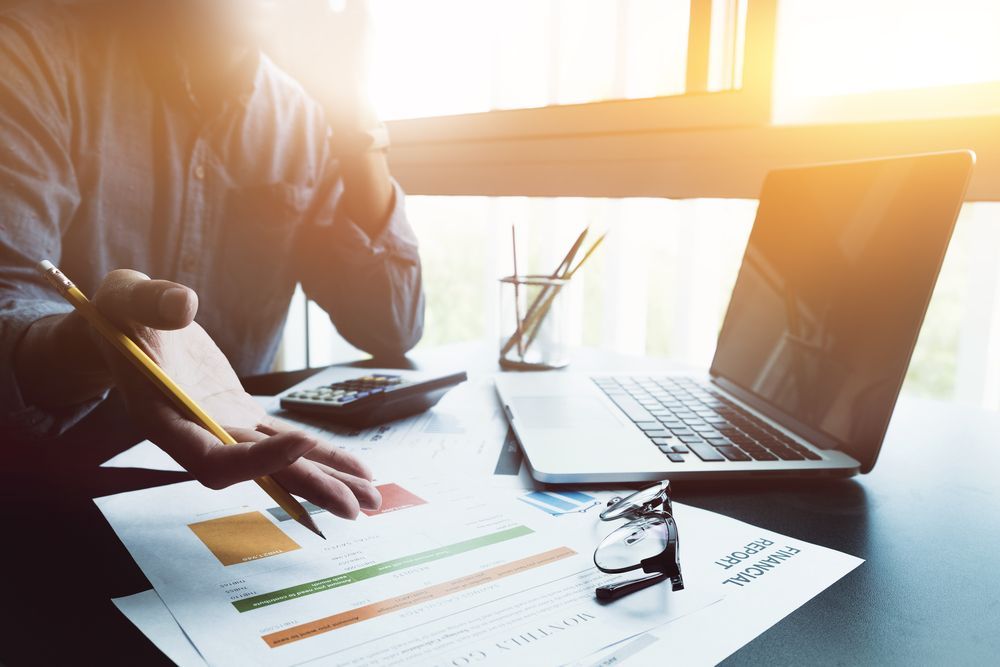 Person Analyzing Financial Reports with A Laptop, Calculator, and Papers at A Desk — Wright Partners in Dubbo, NSW