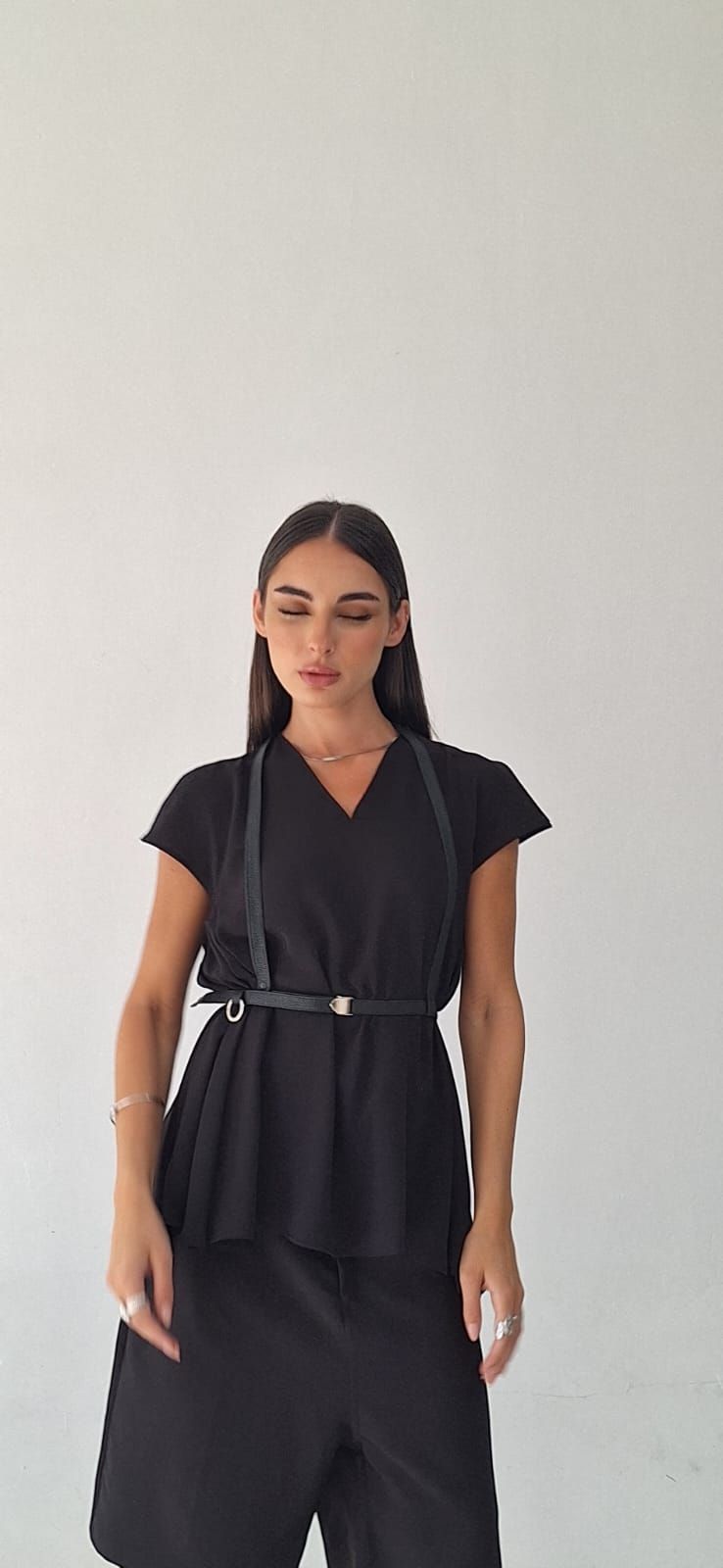 Mujer vestida de negro, con arnés y cinturón, de pie frente a un fondo blanco.