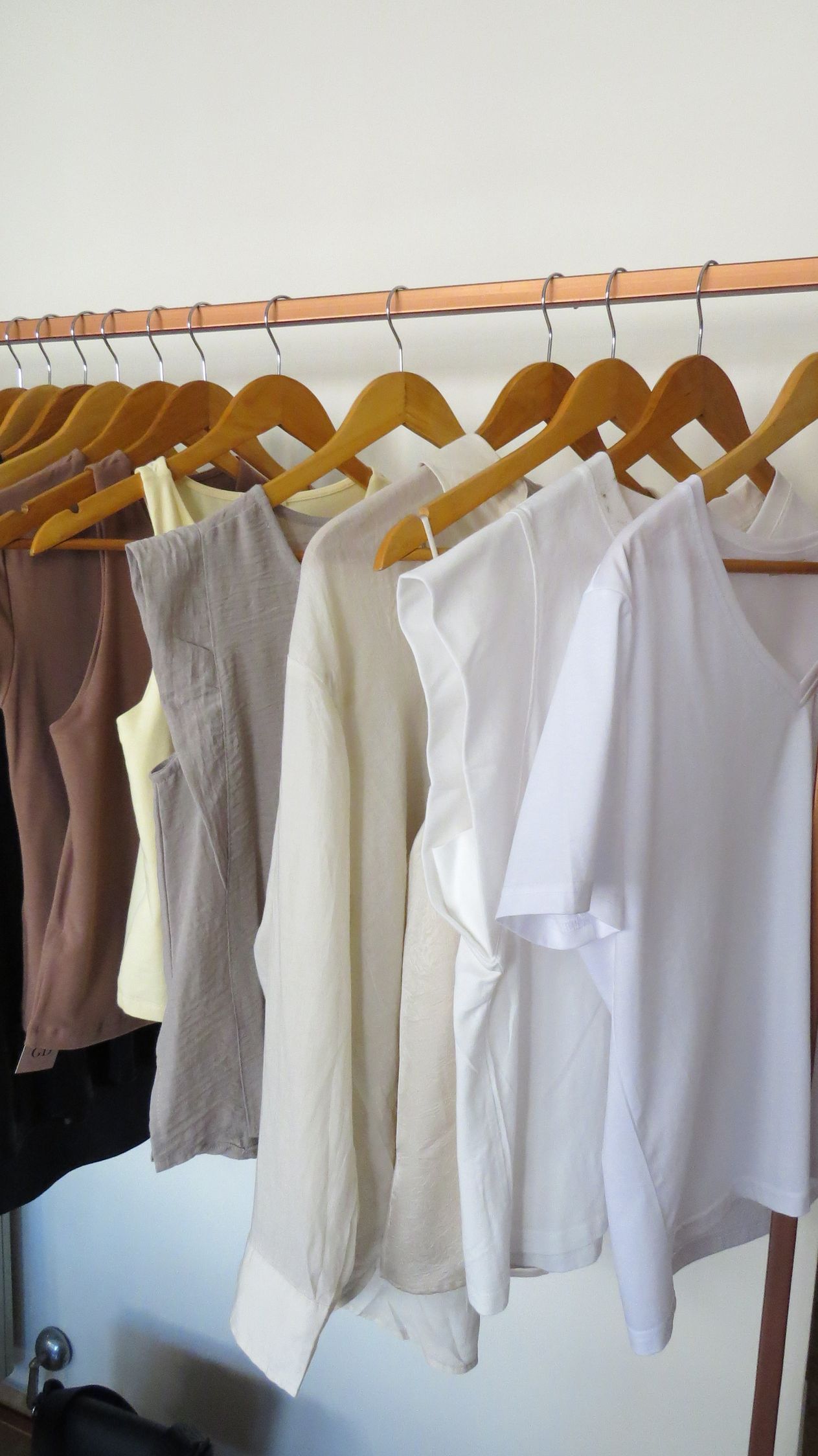 Perchero con varias tapas de colores neutros colgado en perchas de madera.