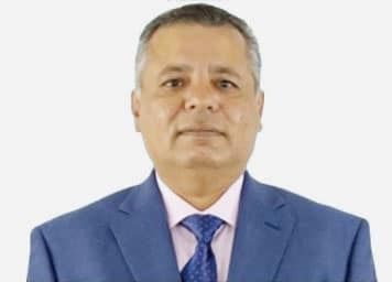 A man in a blue suit, light shirt, and patterned blue tie looking directly at the camera against a white background.