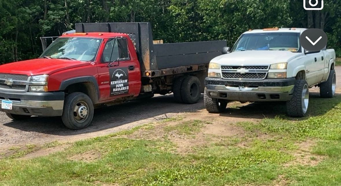 Red and silver pickup trucks parked on grass. Red truck has a flatbed.