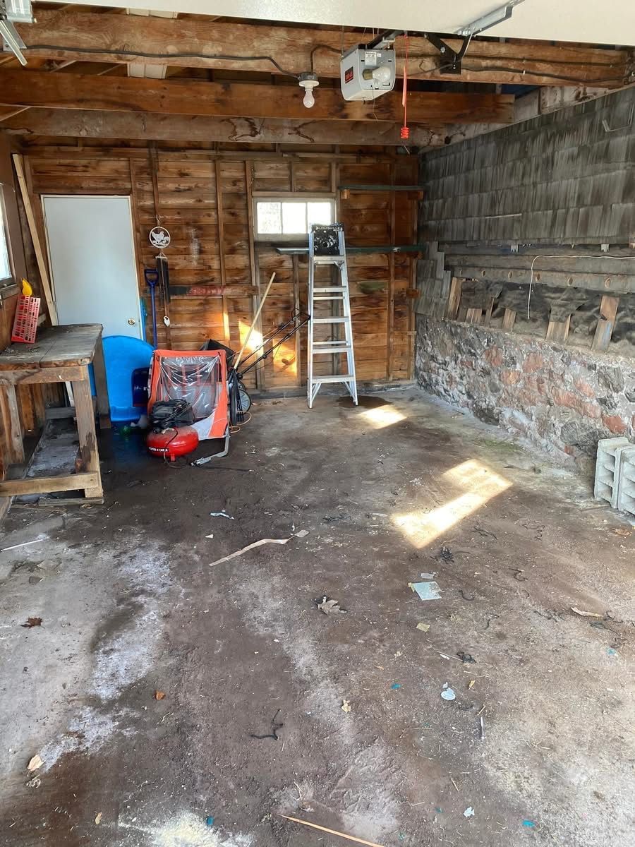 Garage interior under renovation; exposed walls, ladder, workbench, and debris on the floor.