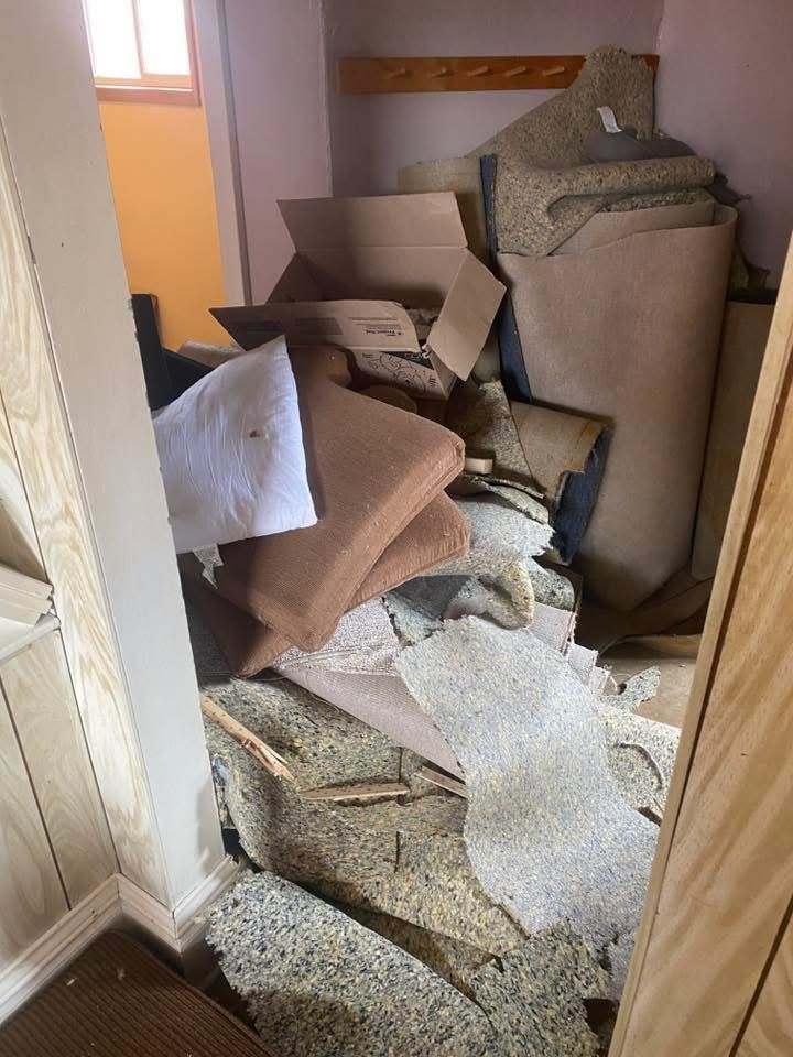 Pile of discarded materials and debris in a hallway, including cardboard, carpet, and pillows.