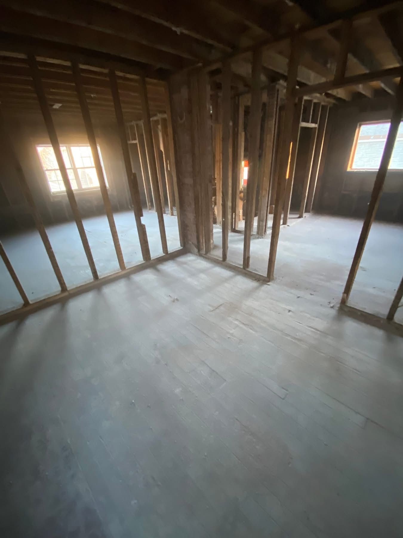 Interior framing of a room with sunlight streaming through windows. Bare wood studs on a gray floor.