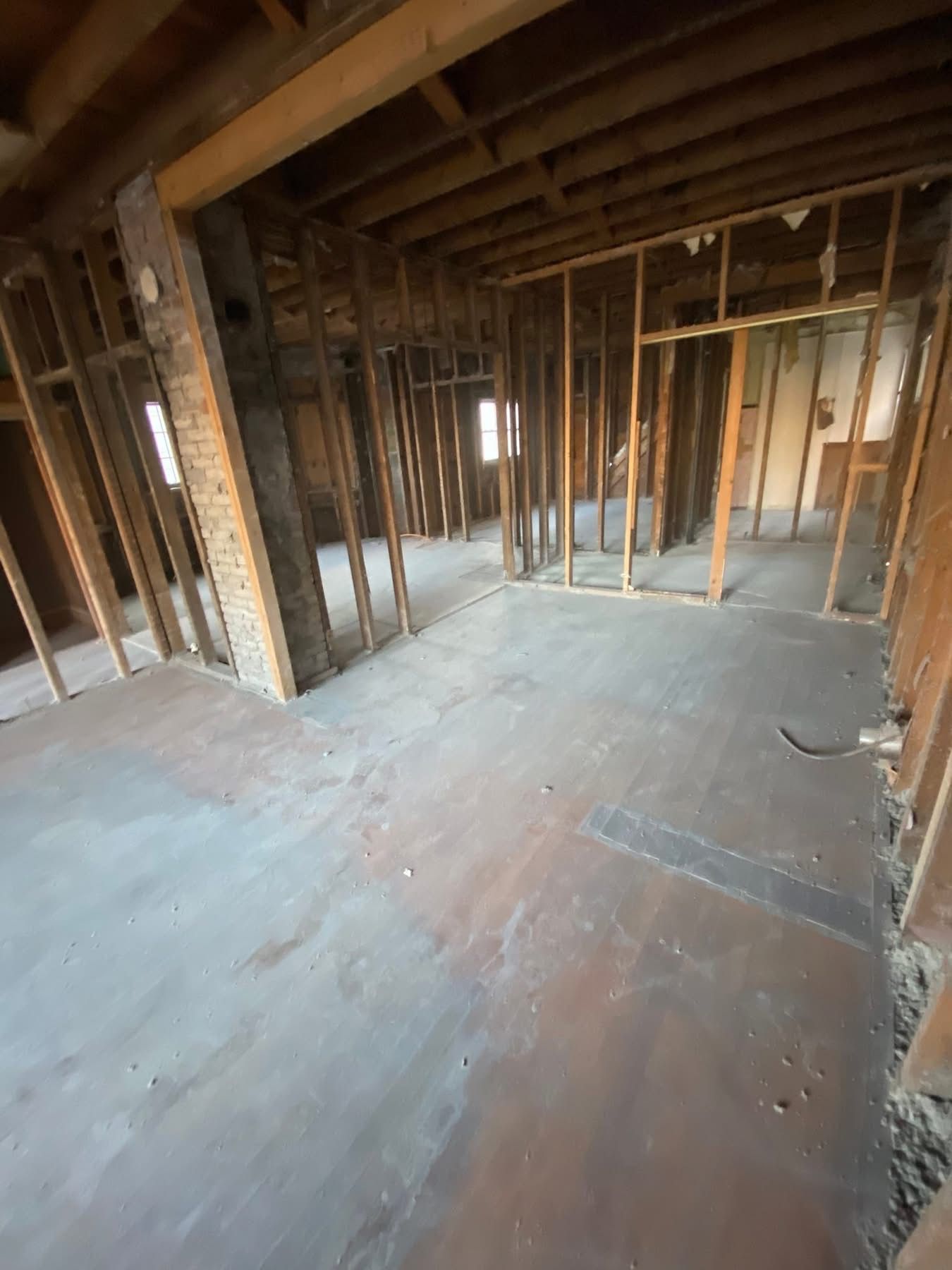 Interior view of a building in demolition. Exposed wooden framing, bare floors, and brick columns are visible.