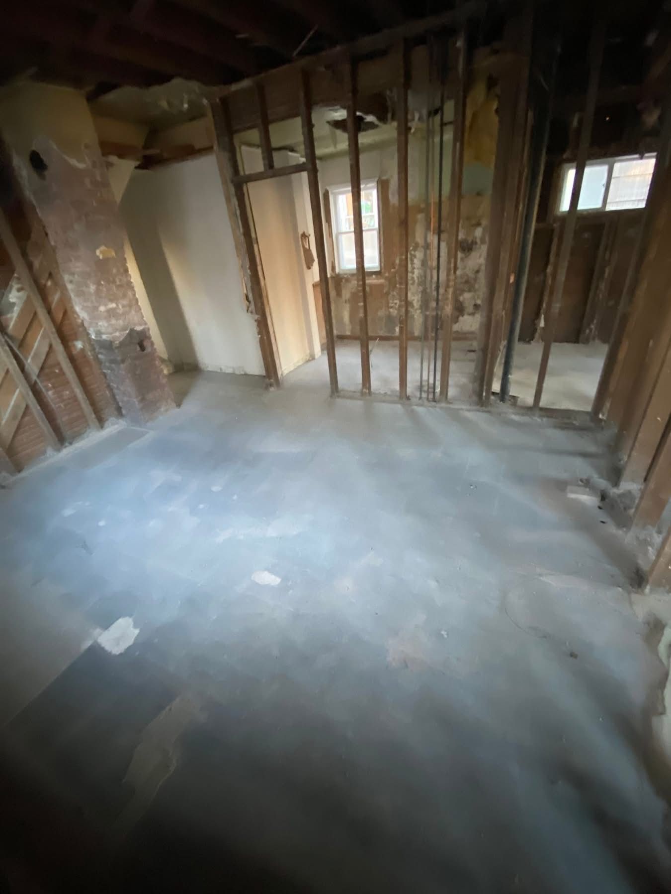 Interior room undergoing renovation, exposed wood framing, concrete floor, doorway to other rooms.