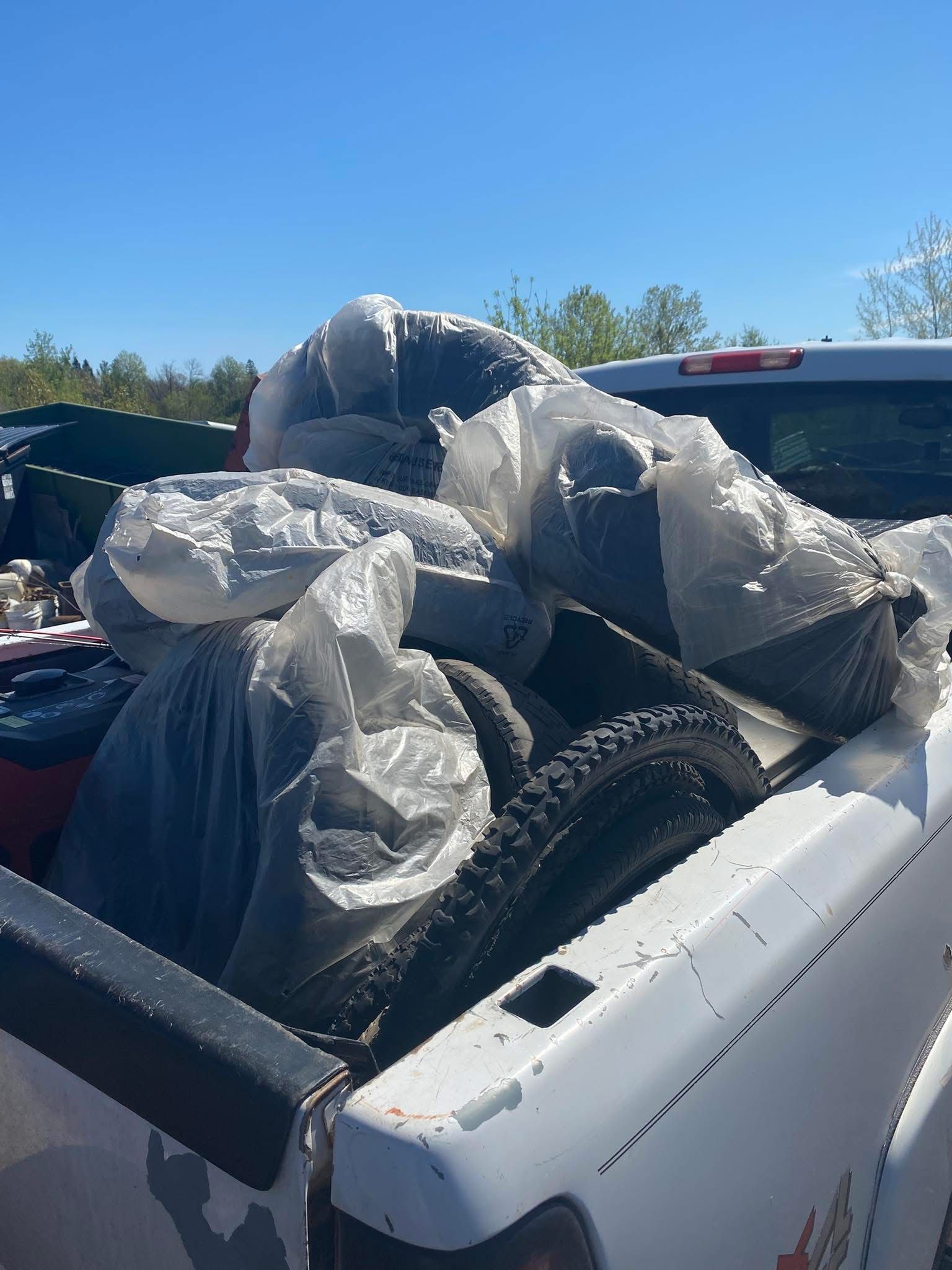 White pickup truck bed filled with plastic bags of black tires, against a blue sky.