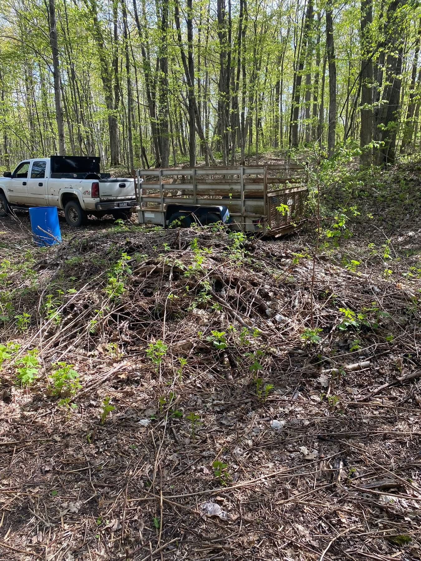 White truck and trailer in woods, near a large pile of leaves.