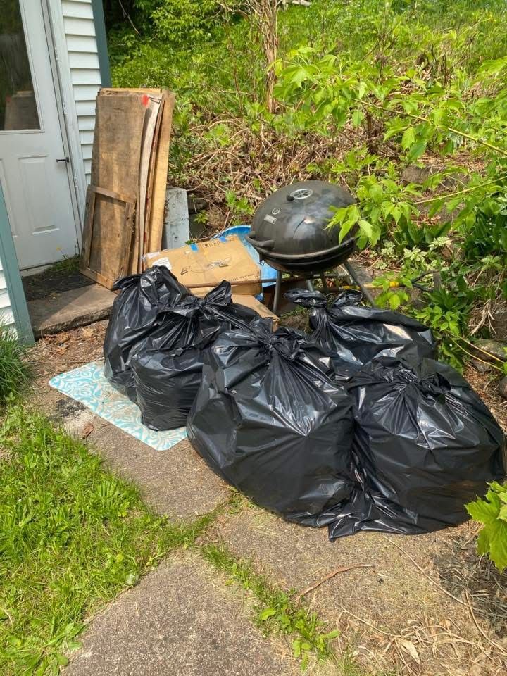 Four black trash bags on a concrete slab near a grill and a door.