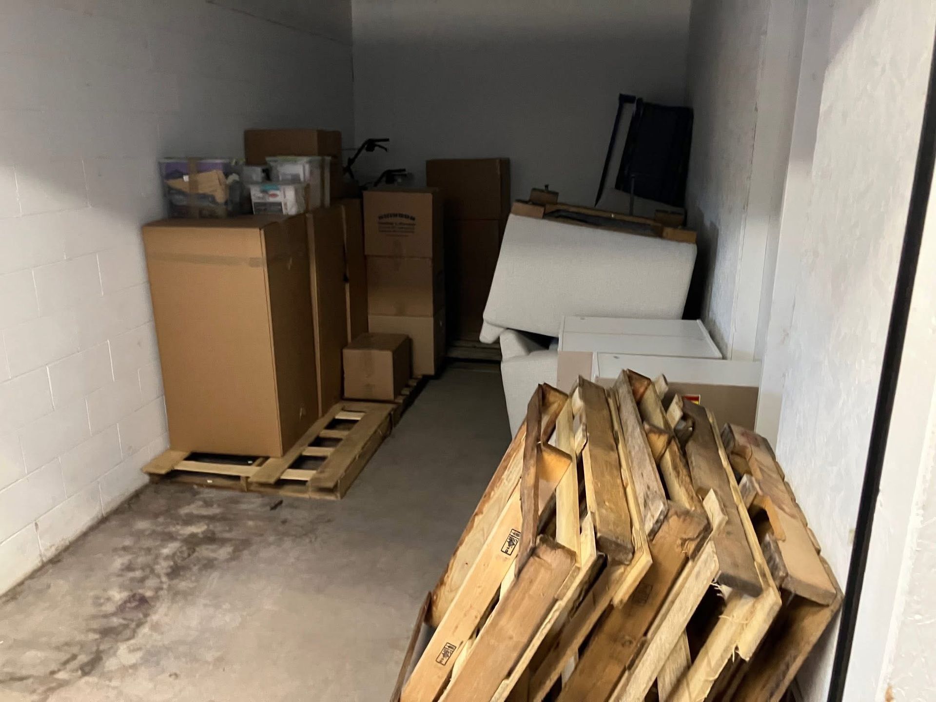 Storage room with cardboard boxes and wooden pallets against white walls.