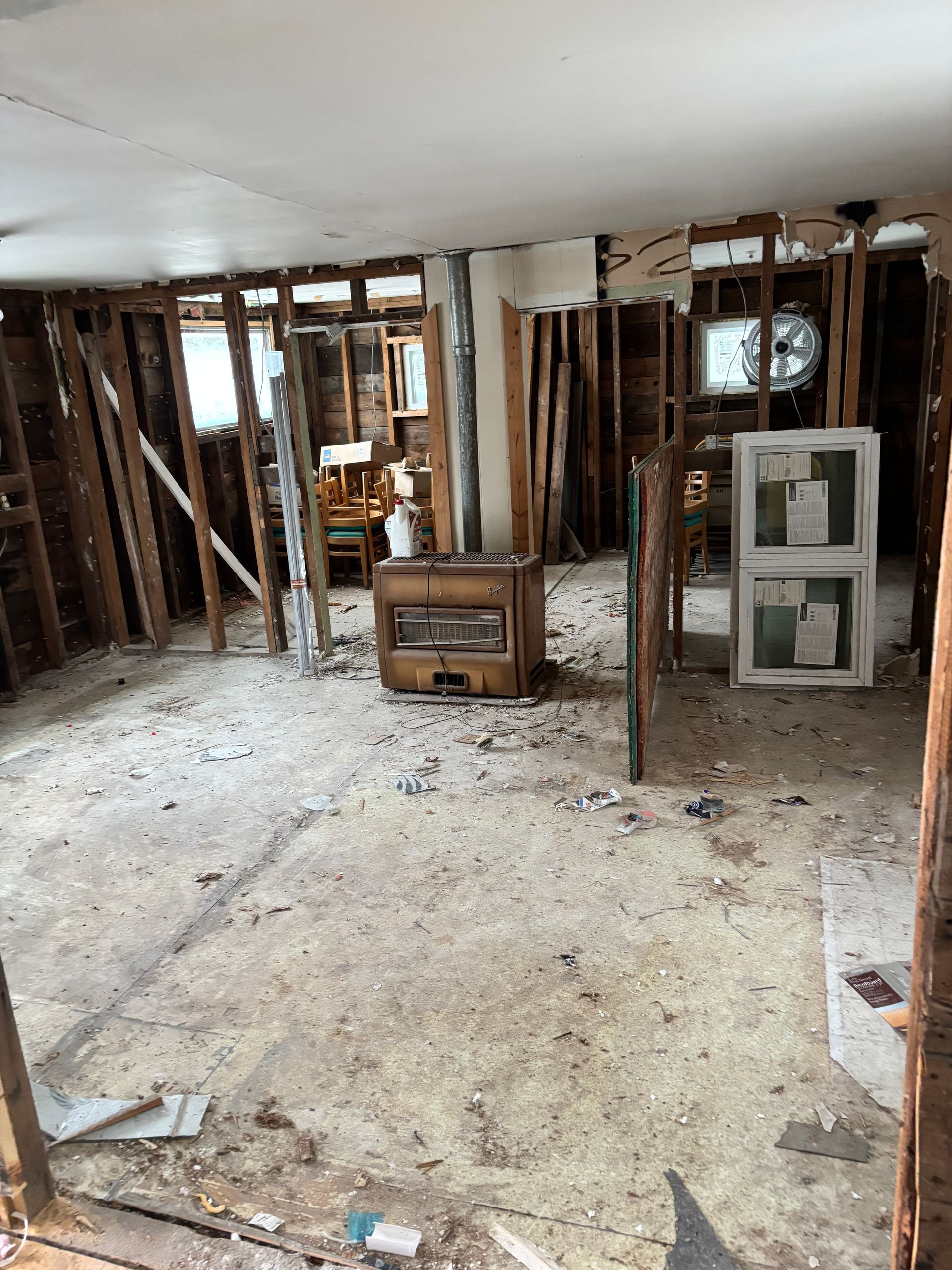 Room under construction; exposed wooden studs, debris on floor, window frames leaning.