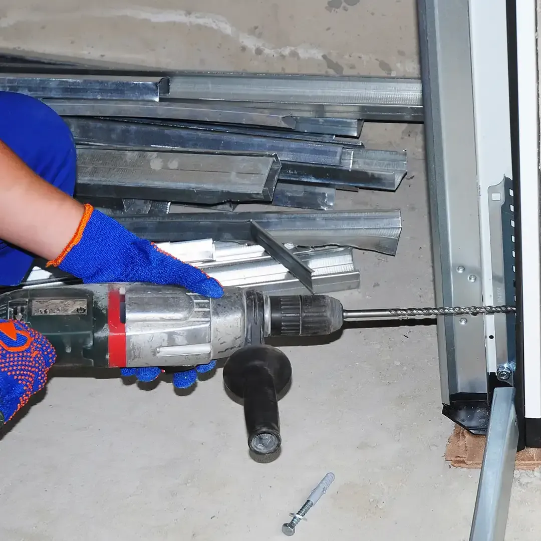 A person wearing blue gloves uses a power drill to install metal brackets for a frame against a wall.