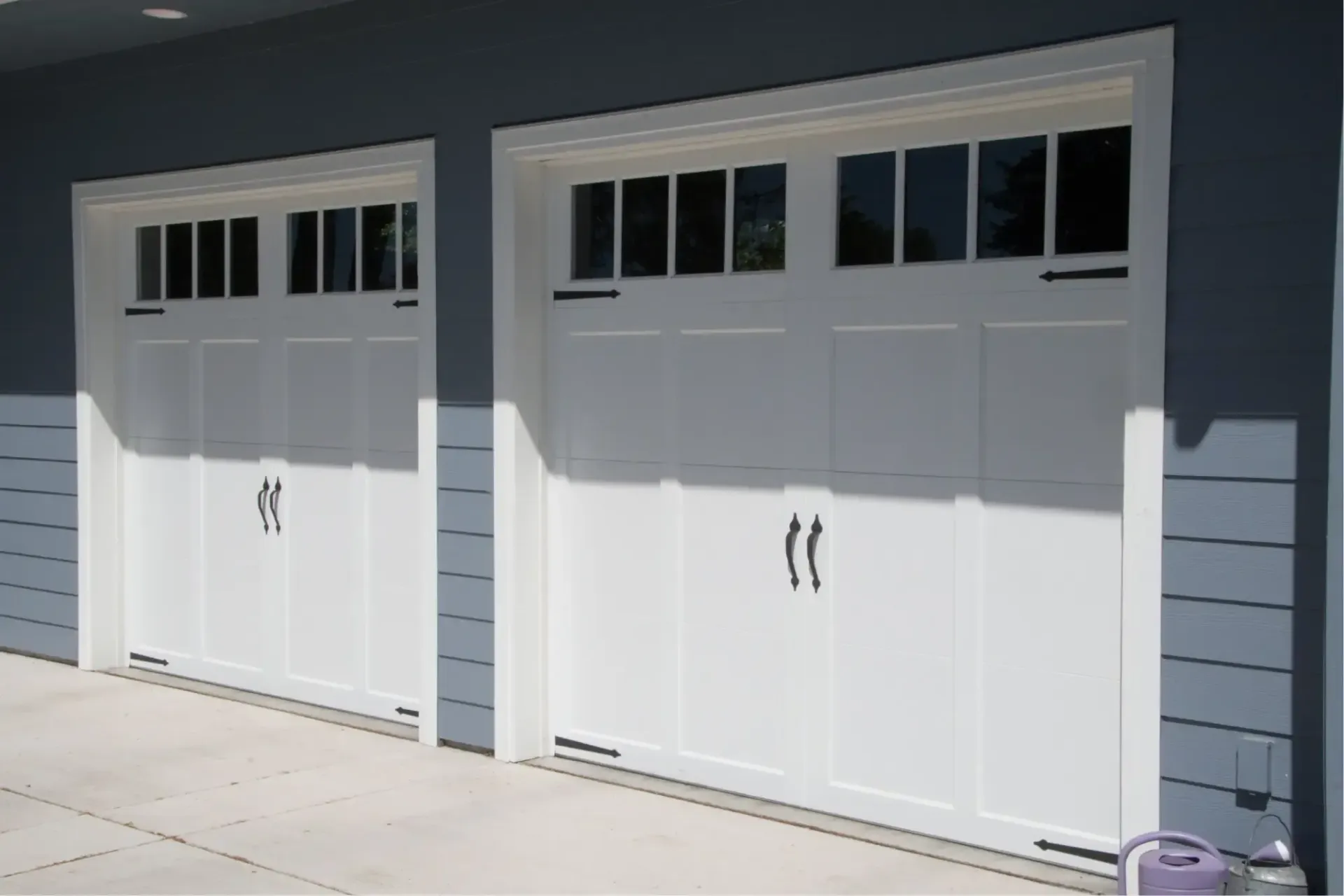 Two white garage doors on a gray house with small windows above each door