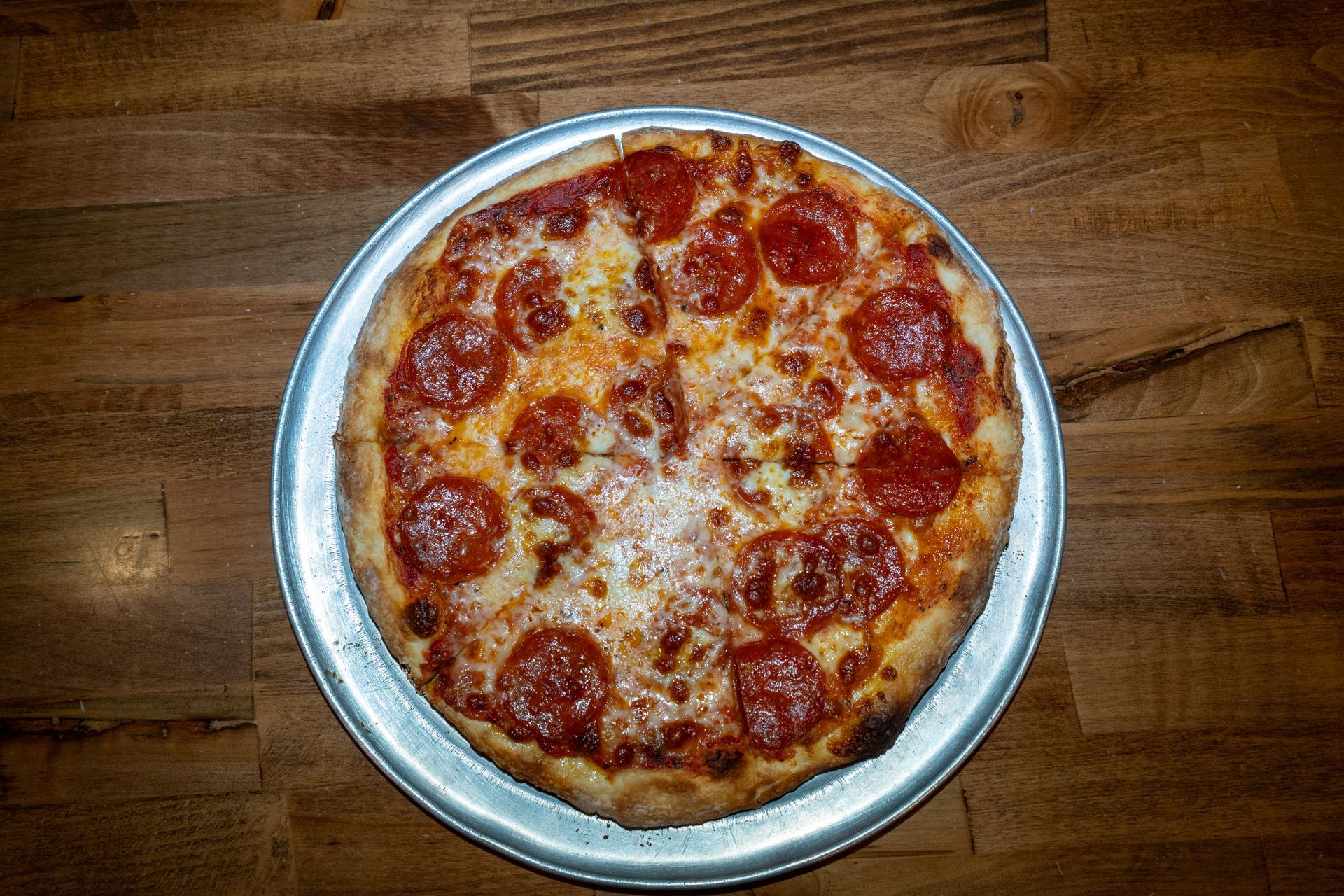 Pepperoni pizza on a silver tray, set on a wooden table.