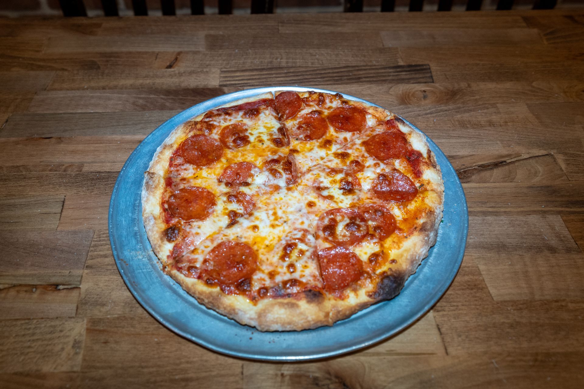 Pepperoni pizza on a silver platter, set on a wooden table.