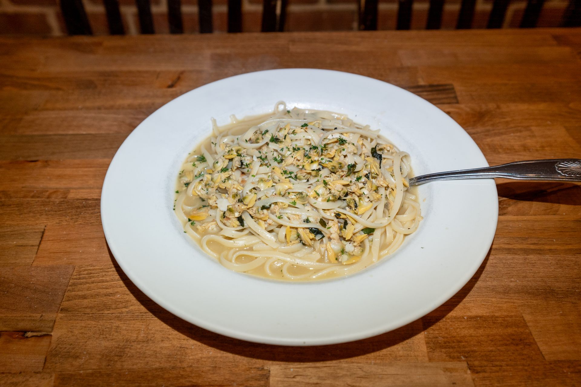 Spaghetti with a garnish of parsley and other toppings on a white plate, wooden table.