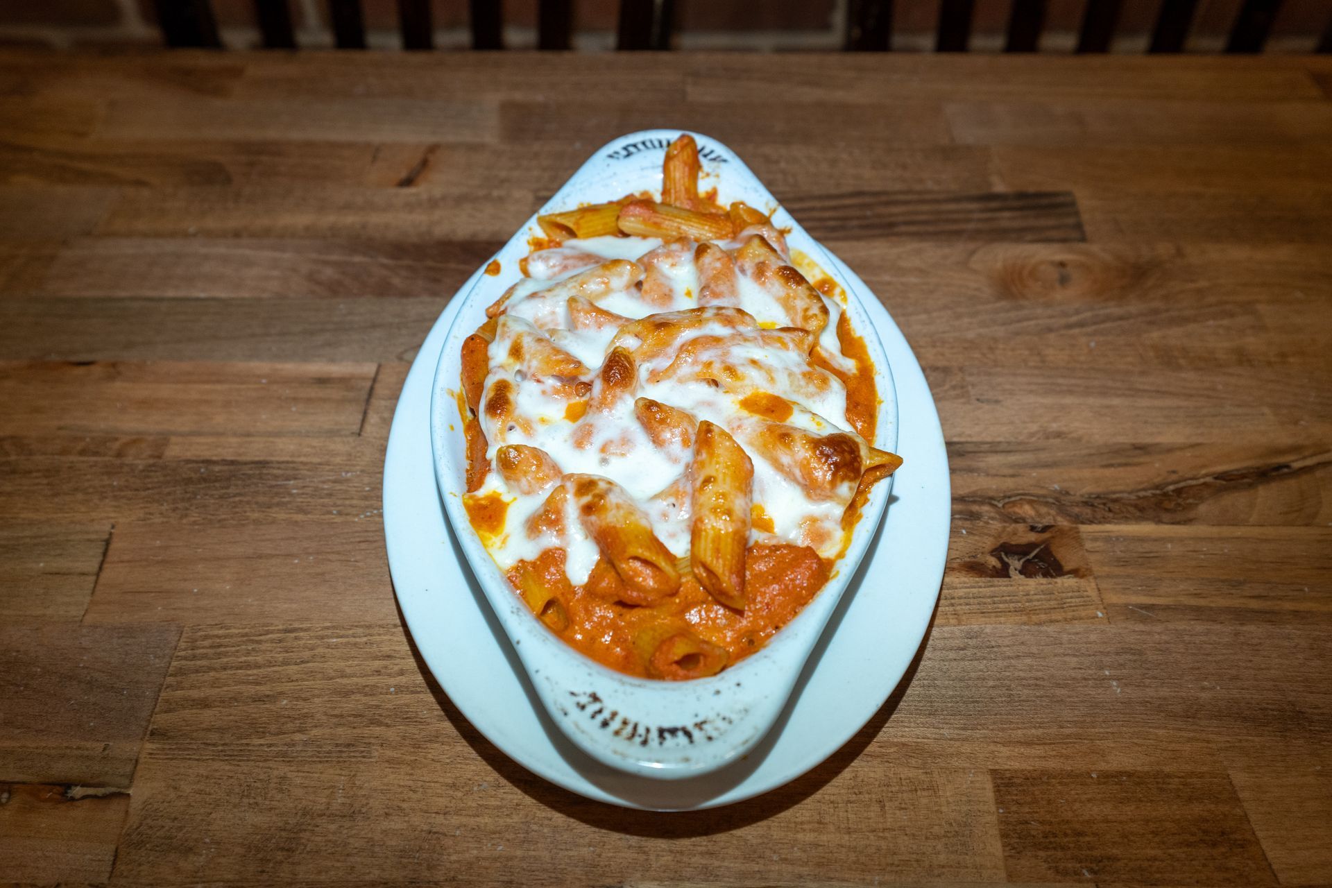 Baked penne pasta in a white serving dish on a wooden table.