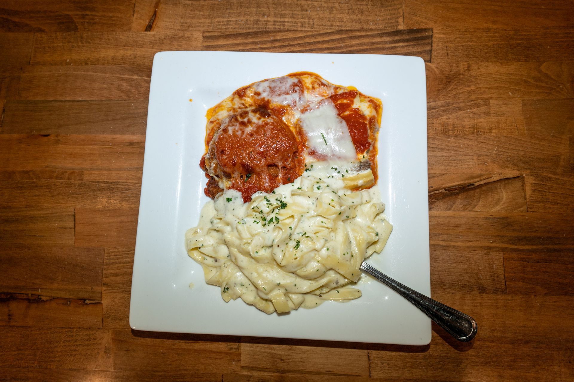 Pasta dish with meatballs and cheese on a white square plate, on a wood table.