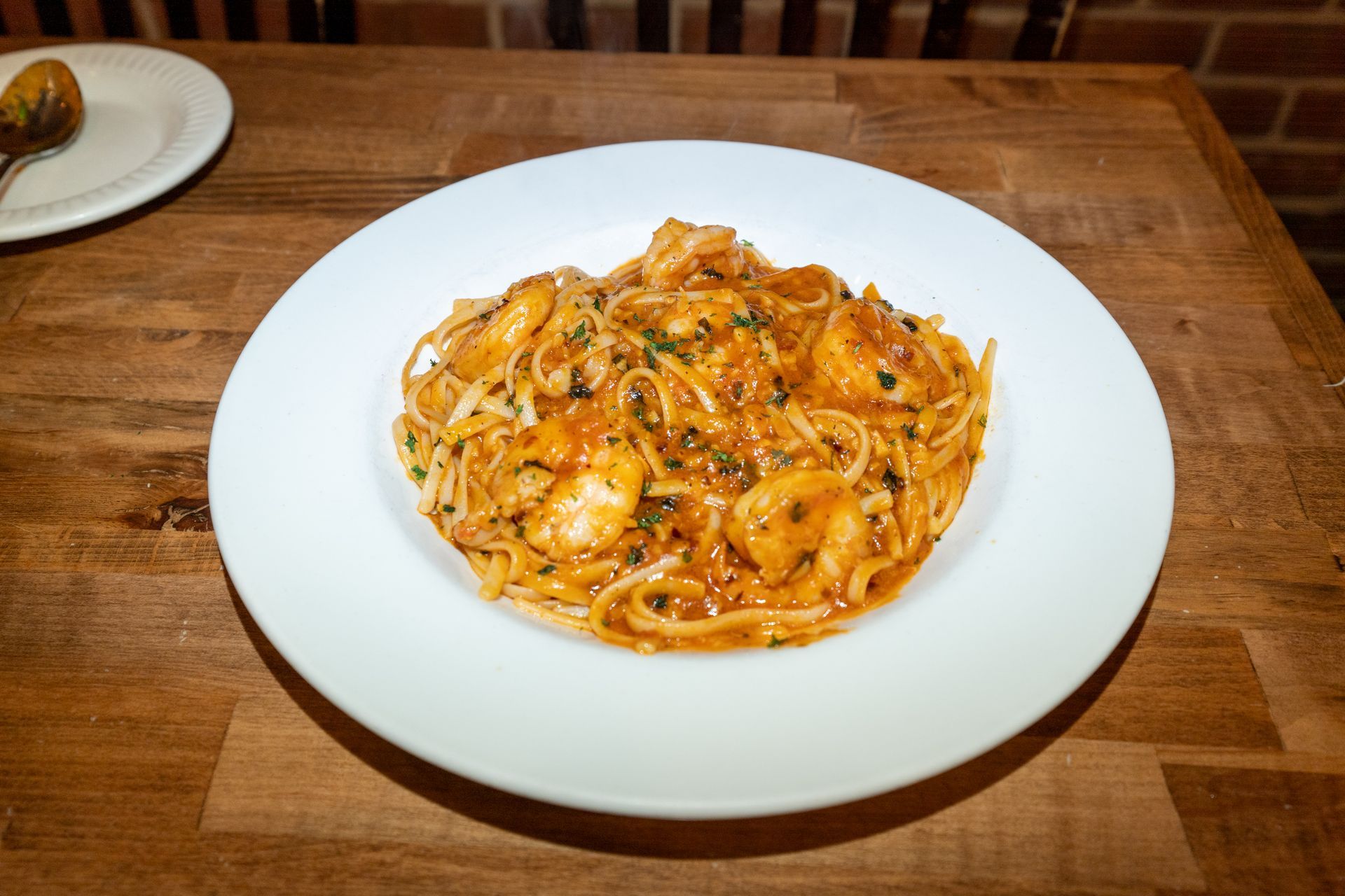 Pasta with shrimp in a tomato sauce, served on a white plate on a wooden table.