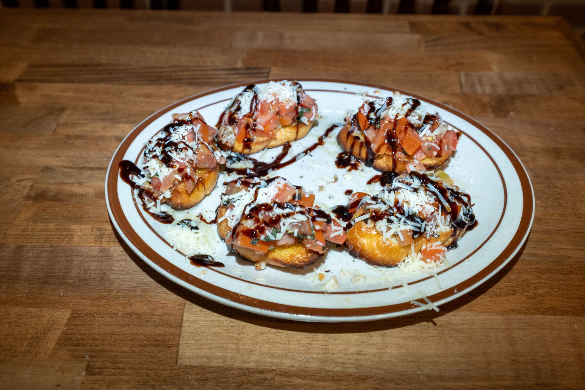 Plate of bruschetta, topped with tomatoes, cheese, and balsamic glaze on a wooden table.