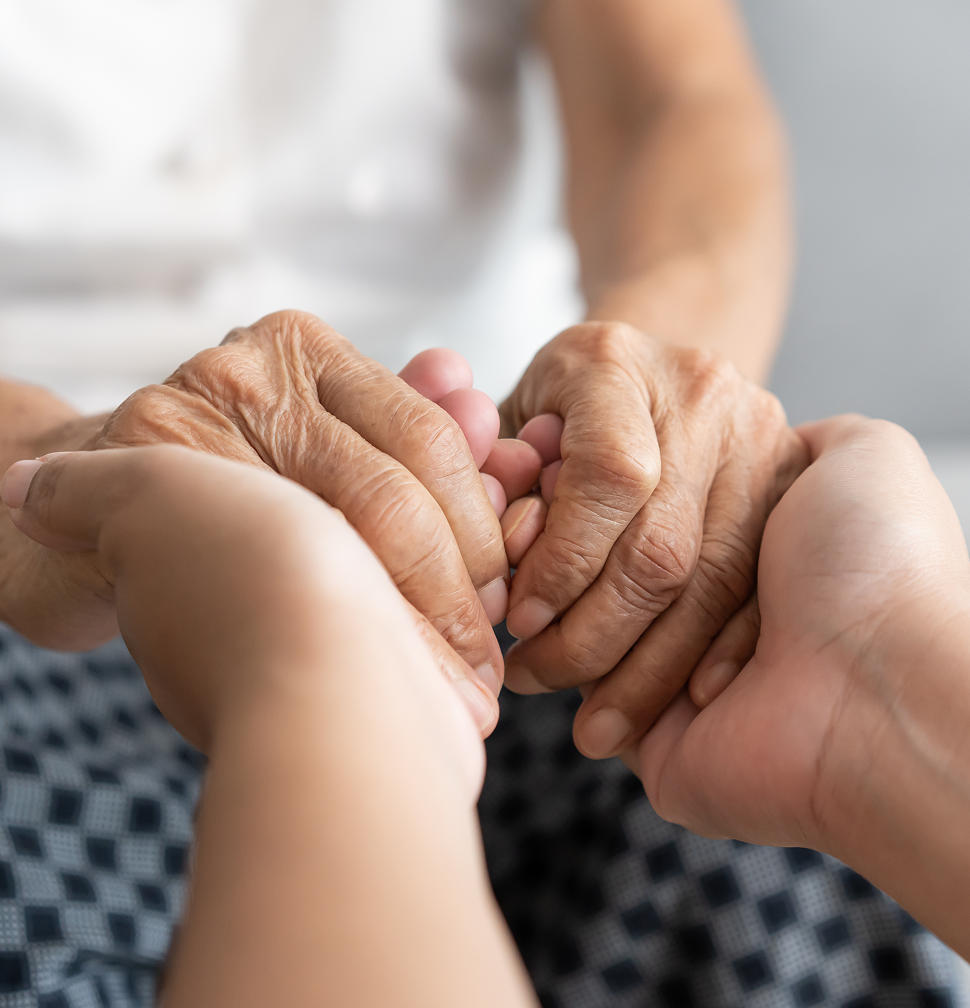 A younger person's hands gently hold an older person's hands, offering comfort and support.