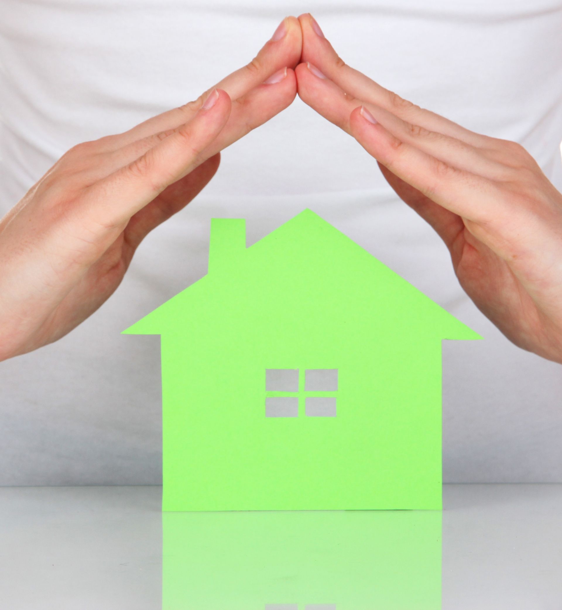 Hands forming a roof shape over a green paper house.