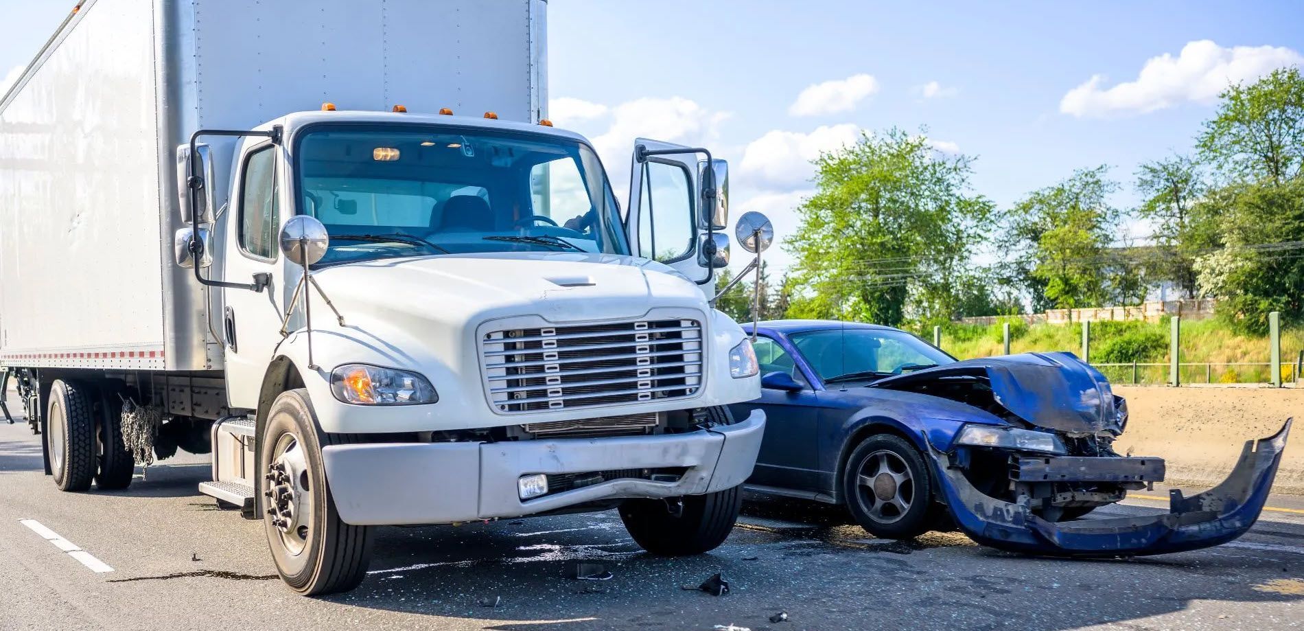 A white semi-truck and a blue car have collided on a highway.