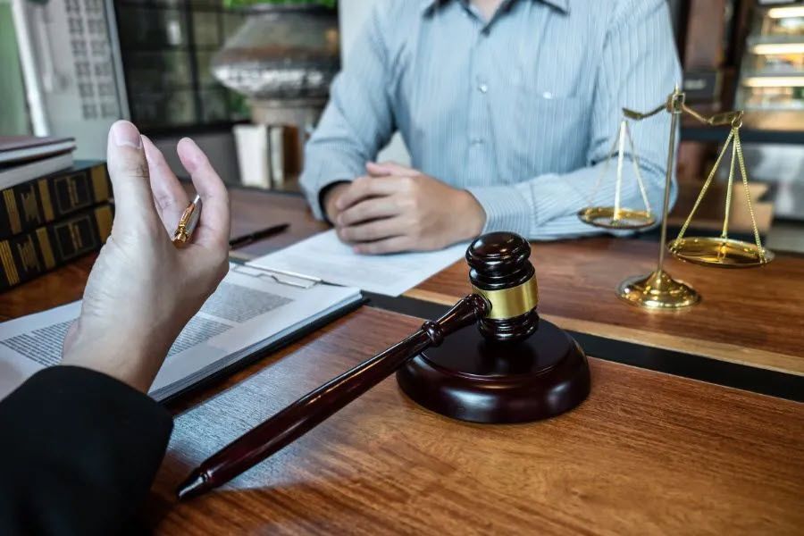 Lawyer discussing documents with a client; scales of justice and gavel on wooden table.