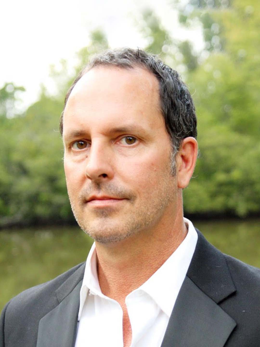 A man in a suit and white shirt is looking at the camera