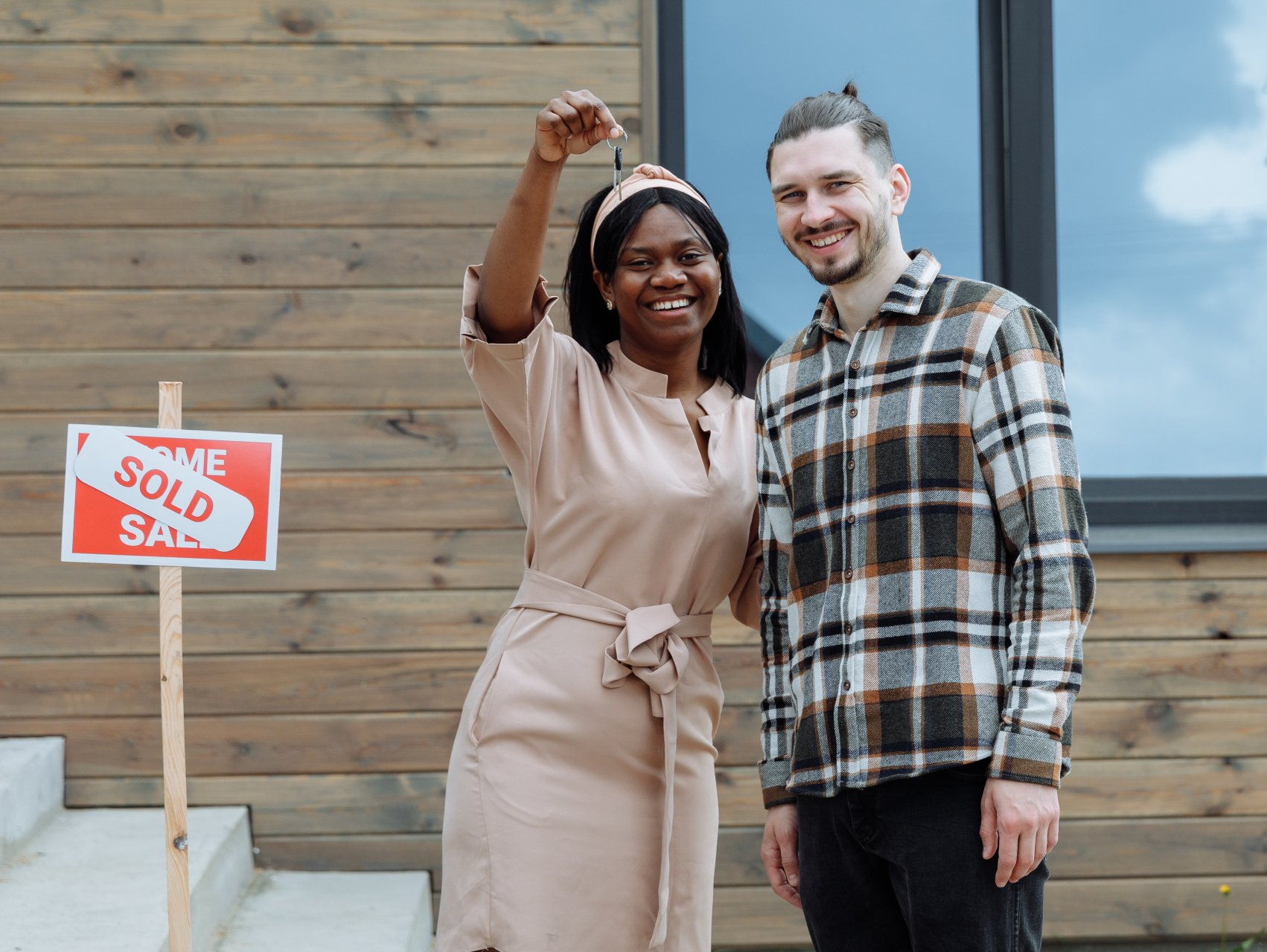 A man and a woman are standing in front of a house with a sold sign.