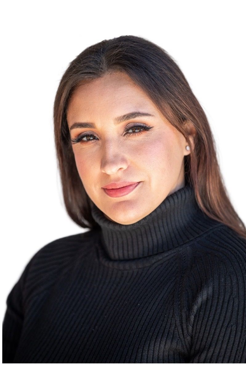 A woman wearing a black turtleneck sweater is standing in front of a white background.